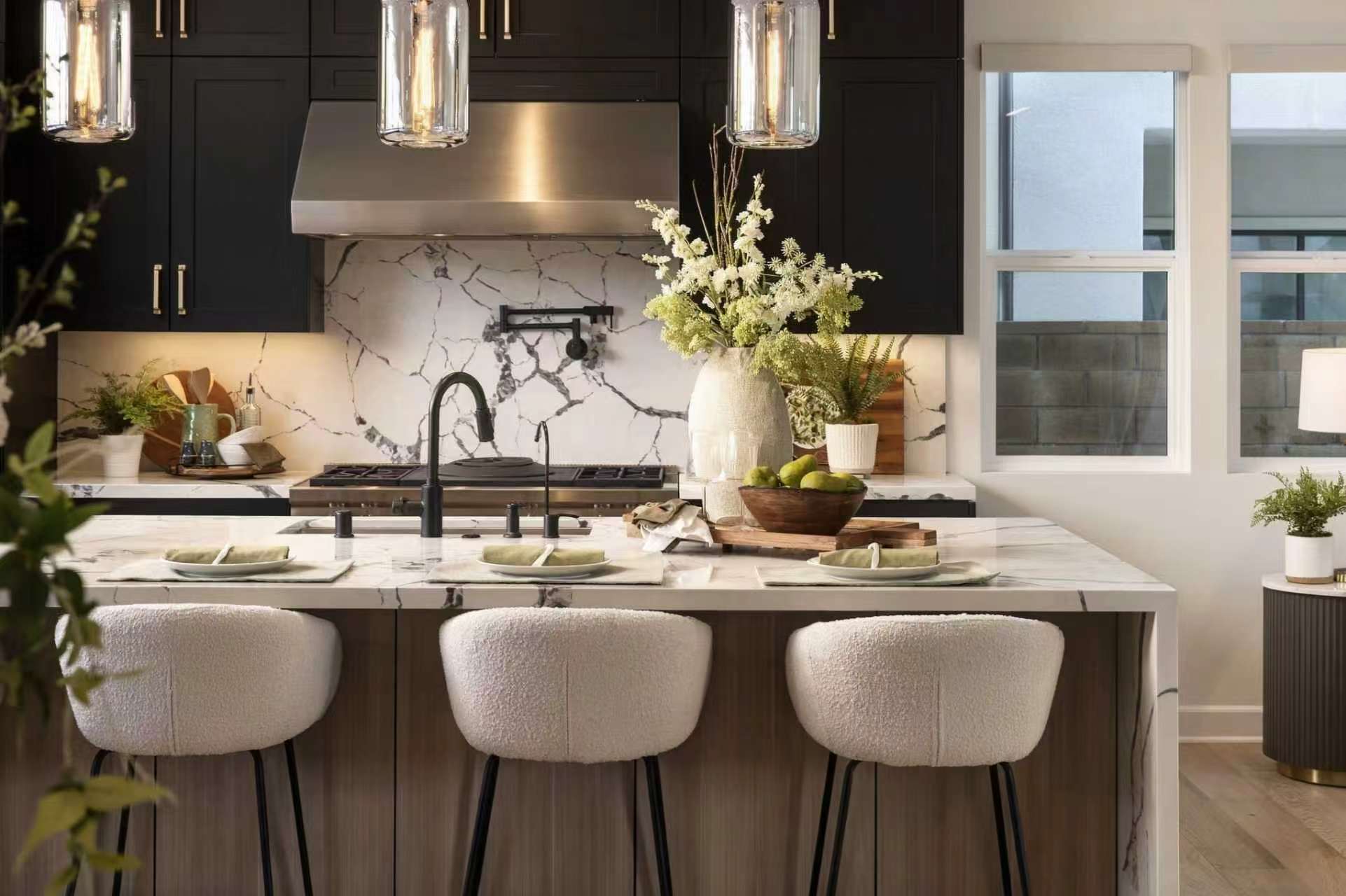 Kitchen with dark cabinets, veined stone island, glass pendant lights and upholstered stools