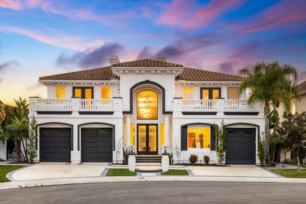 White two-story home with illuminated windows beneath a pink and blue evening sky